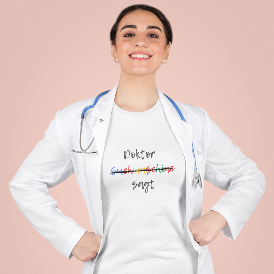 Gut gelaunte Ärztin mit Kittel und Stethoskop trägt mit Humor und Aussagekraft ihr Organic T-Shirt mit dem Aufdruck Doktor sagt, nicht Suchmaschine sagt. Im Krankenhaus, in der Praxis oder im Alltag ist dieses Mediziner Shirt toll zu tragen.  
